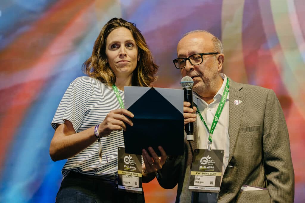 Dupla anunciando um prêmio ao microfone em evento de inovação